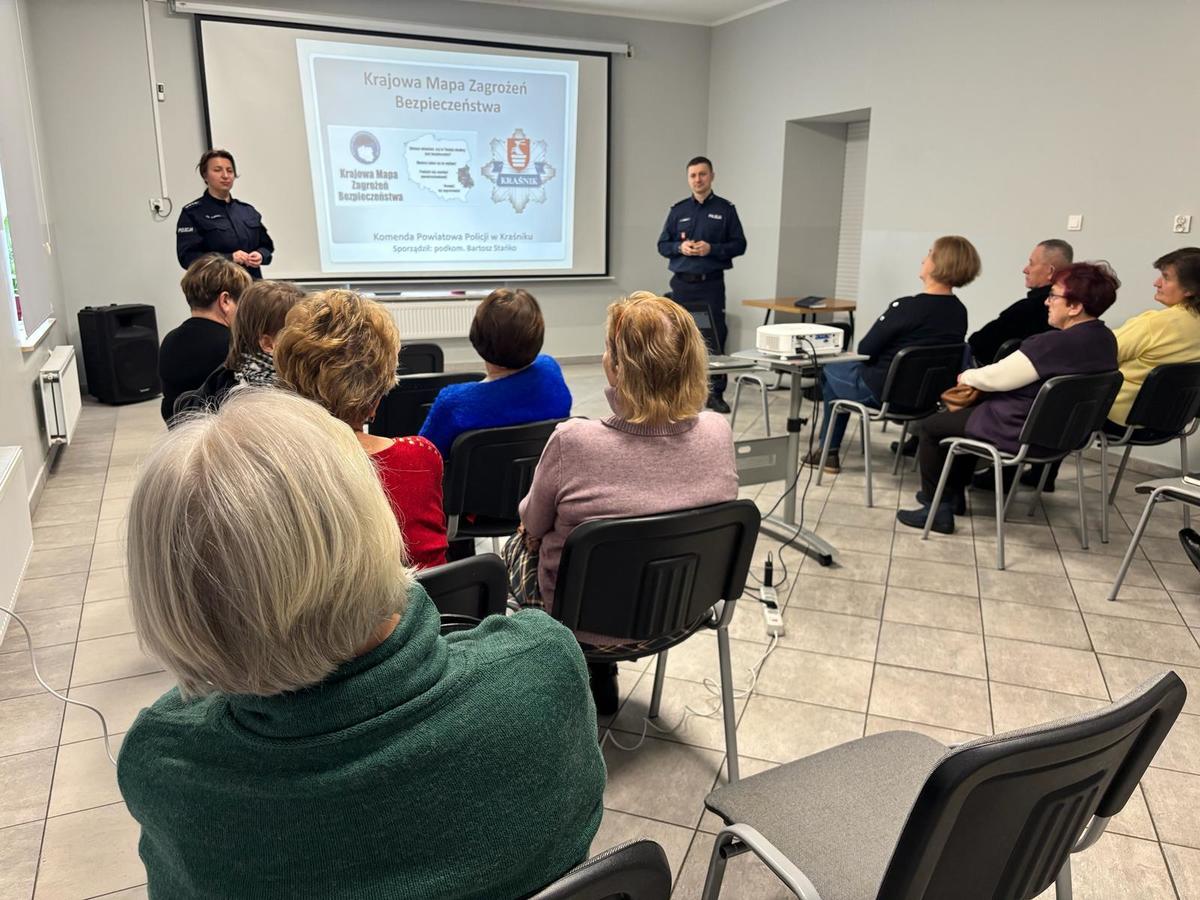 zastępca komendanta powiatowego policji w krasniku oraz policjantka wydziału prewencji stoją przy tablicy multimedialnej przed gronem osób siedzących na krzesłach