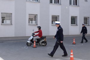 Zdjęcie przedstawia uczestnika turnieju na motorowerze , policjant nadzorujący prawidłowy przejazd