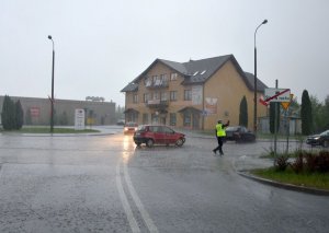 Zdjęcie przedstawia Policjanta kierujący ruchem na drodze, widoczny uszkodzony samochód