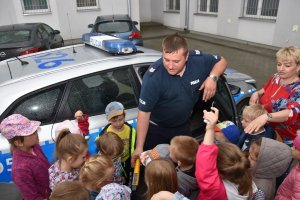 Zdjęcie przedstawia przedszkolaki z wychowawcą przy radiowozie oraz policjanta, który z niego wychodzi.