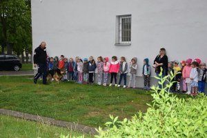 Zdjęcie przedstawia przedszkolaki oraz policjanta z psem policyjnym.