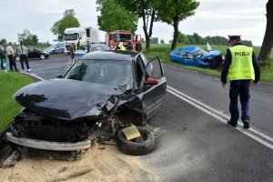 Zdjęcie przedstawia rozbity samochód na miejscu zdarzenia, policjant obsługujący wypadek