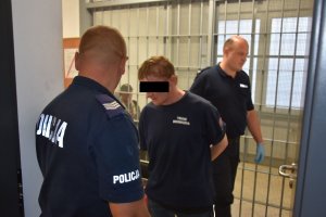 Zdjęcie przedstawia policjantów w komendzie prowadzących czynności z zatrzymanym mężczyzną