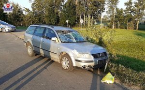 Zdjęcie przedstawia pojazd uczestniczący w zdarzeniu drogowym z uszkodzeniami oraz fragment radiowozu.