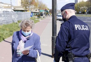 Zdjęcie przedstawia funkcjonariusza Policji wręczającego maseczkę.