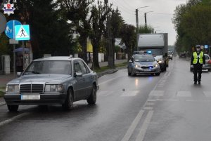 ZDJECIE PRZEDSTAWIA MIEJSCE POTRĄCENIA NA PASACH DROGI, W TLE POJAZDY I POLICJANCI