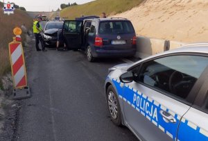 Zdjęcie przedstawia uszkodzone pojazdy i policjanta