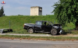 Zdjęcie przedstawia uszkodzony pojazd na trawie po wypadku z boku