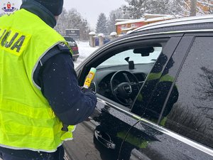policjant stoi przy samochodzie od strony kierowcy z urządzeniem do badania stanu trzeźwości
