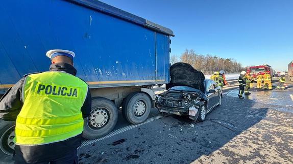 policjant stoi tyłem przy niebieskiej naczepie samochodu ciężarowego, przy tylnym rogu naczepy stoi samochód marki Saab z podniesioną pokrywą silnika