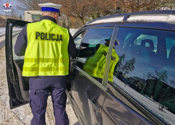 policjant stojący przy otwartych drzwiach samochodu