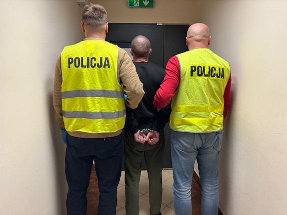 stojący policjanci z zatrzymanym mężczyzną po środku