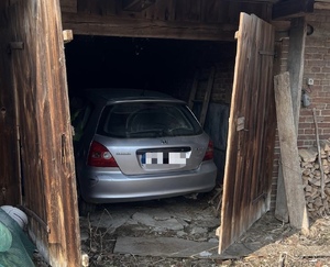 srebrny samochód stoi w budynku gospodarczym z drewnianymi drzwiami