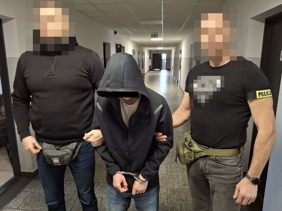 zatrzymany z kajdankami na dłoniach a po bokach stoją policjanci