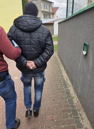 zatrzymany mężczyzna z rękami z tyłu z kajdankami idzie chodnikiem