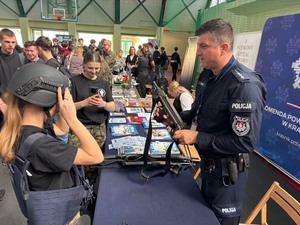 policjant pokazuje kobiecie jak wygląda obsługa broni