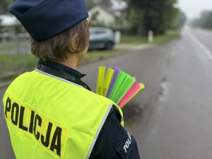 policjantka stoi tyłem widać ją do połowy pasa i trzyma odblaski w rękach