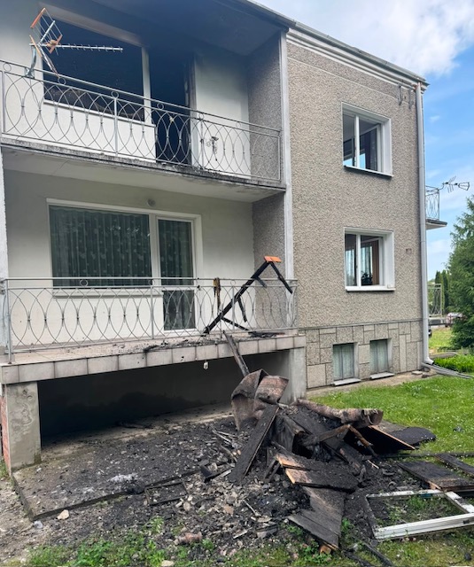 murowany budynek po pożarze przed którym leżą spalone elementy wyposażenia domu