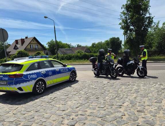 policjanci stojący przy motocyklach po lewej stronie stoi samochód osobowy
