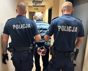 zatrzymany mężczyzna prowadzony przez dwóch policjantów korytarzem