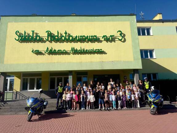 policjanci ruchu drogowego na wspólnym grupowym zdjęciu z dziećmi pod szkołą