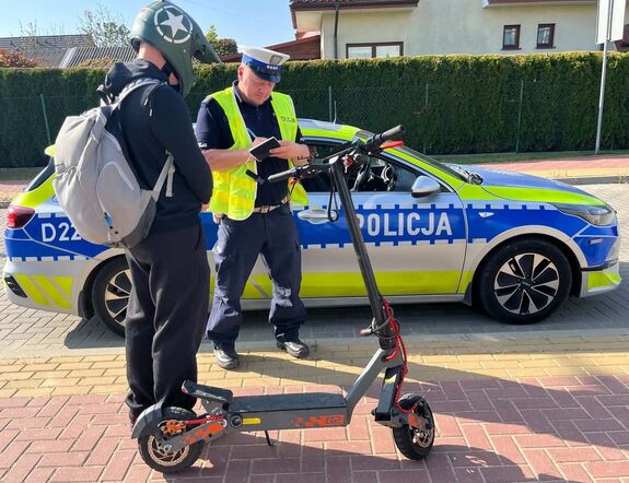 policjant stoi przy radiowozie a obok niego mężczyzna i hulajnoga