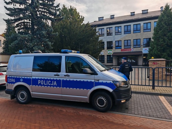 radiowóz policyjny stoi przy ogrodzeniu szkoły obok jest policjant