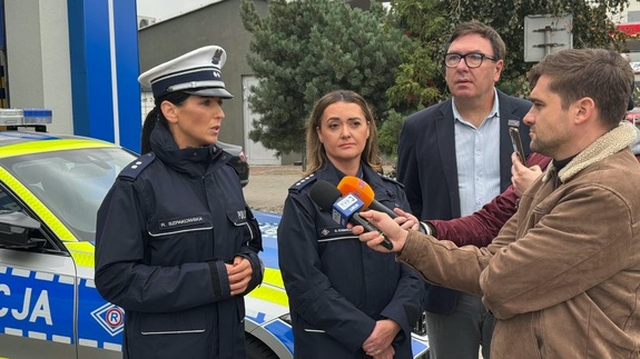od lewej strony stoją dwie policjantki po prawej widoczni reporterzy z mikrofonami