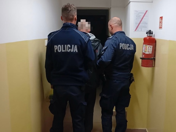 zatrzymany prowadzony przez dwóch policjantów w korytarzu budynku