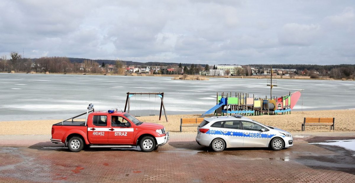 Widok na zalew, w tle radiowozy straży i policji 